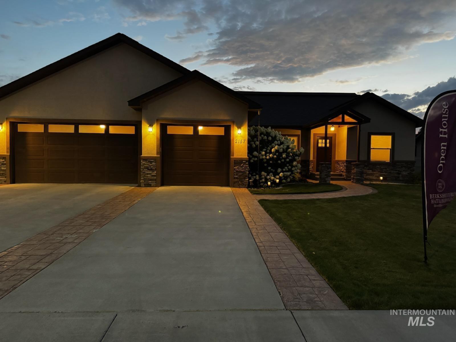 View of front facade with a garage, stone siding, stucco siding, concrete driveway, and a front lawn