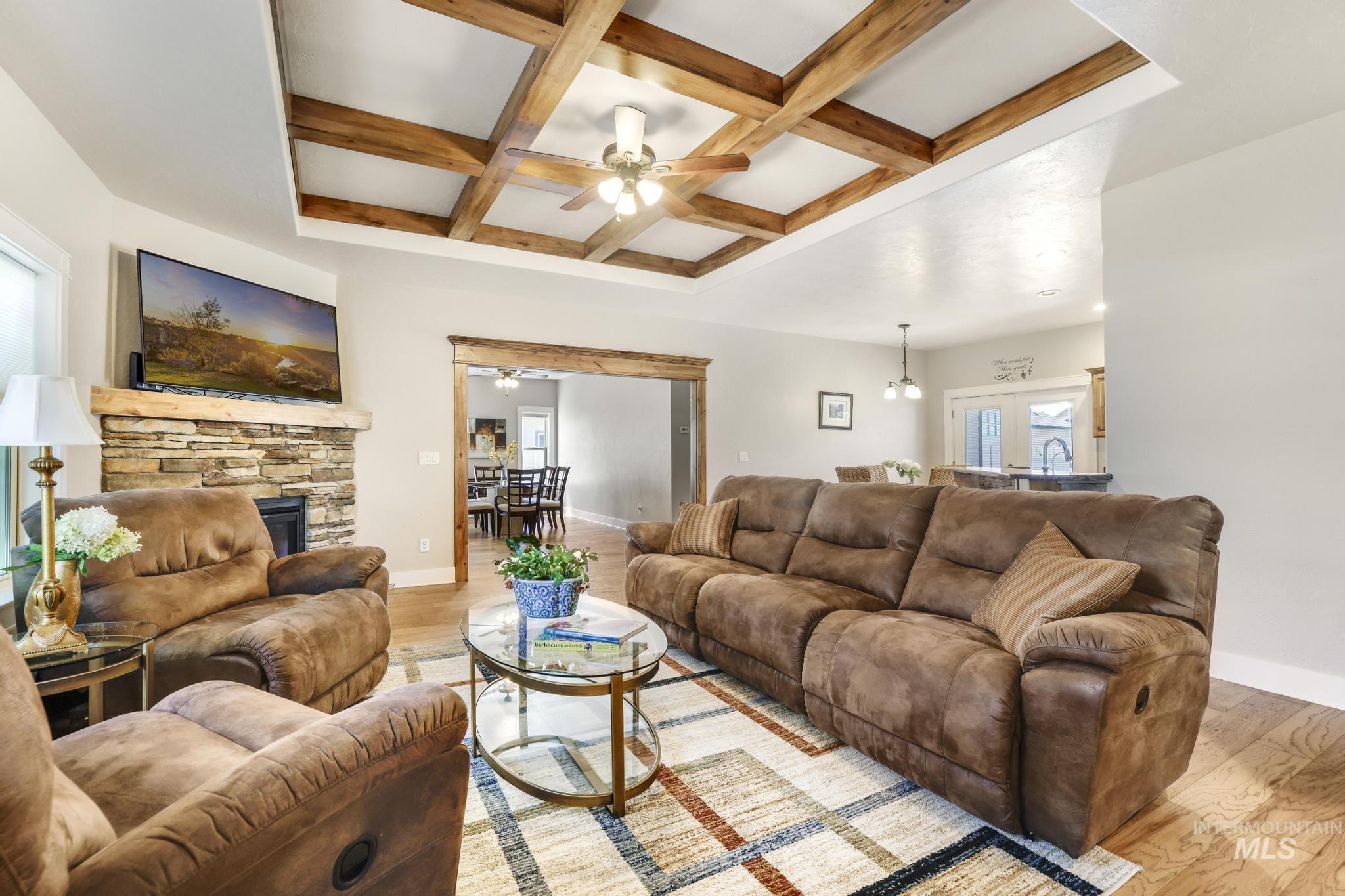 Living area featuring coffered ceiling, a ceiling fan, beamed ceiling, light wood-type flooring, and a fireplace