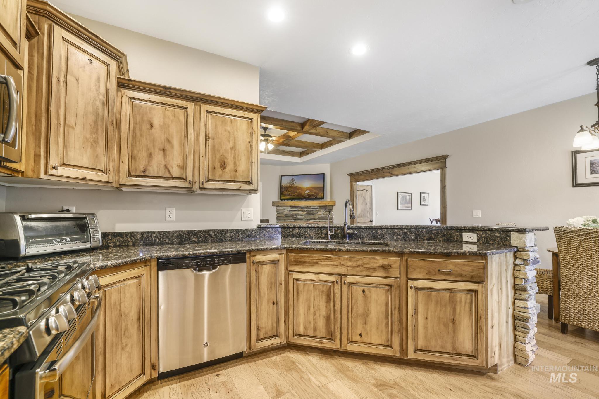 Kitchen with dark stone countertops, appliances with stainless steel finishes, a peninsula, brown cabinetry, and light wood-style flooring