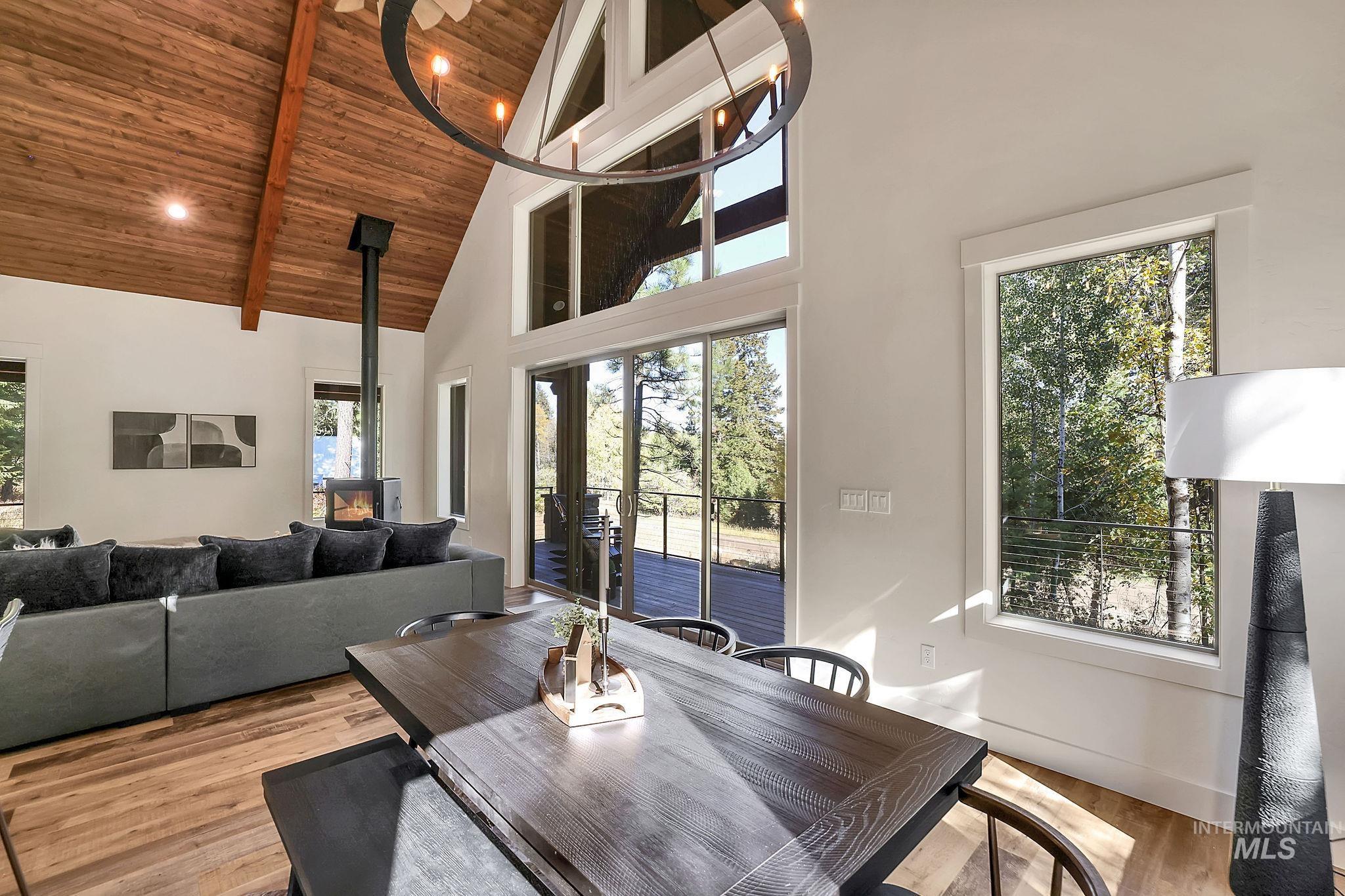 Dining room with a wood stove, wood finished floors, high vaulted ceiling, a wooden ceiling with exposed beams, and healthy amount of natural light