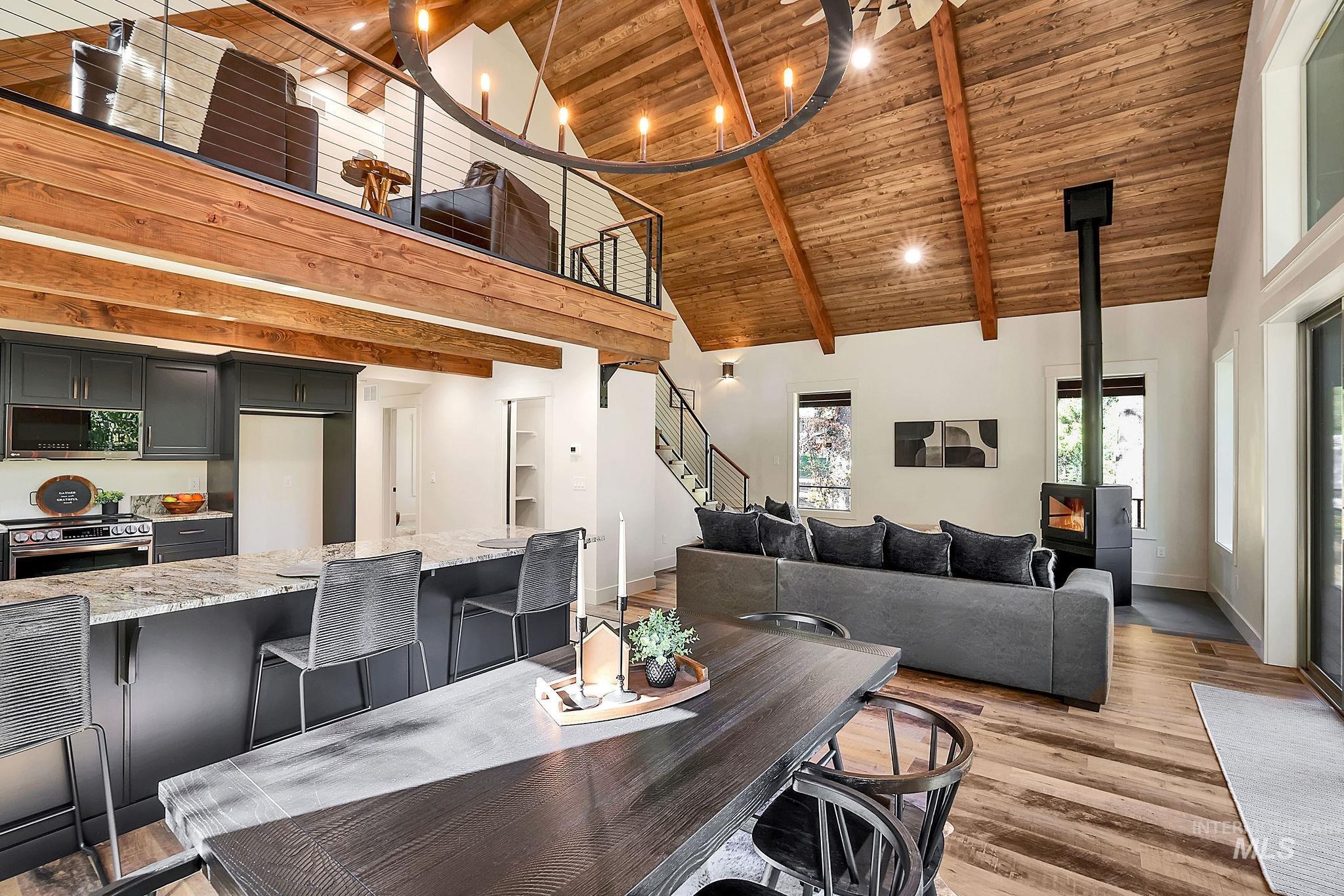 Dining room with high vaulted ceiling, a wood ceiling with exposed beams, a wood stove, light wood-style flooring, and stairs