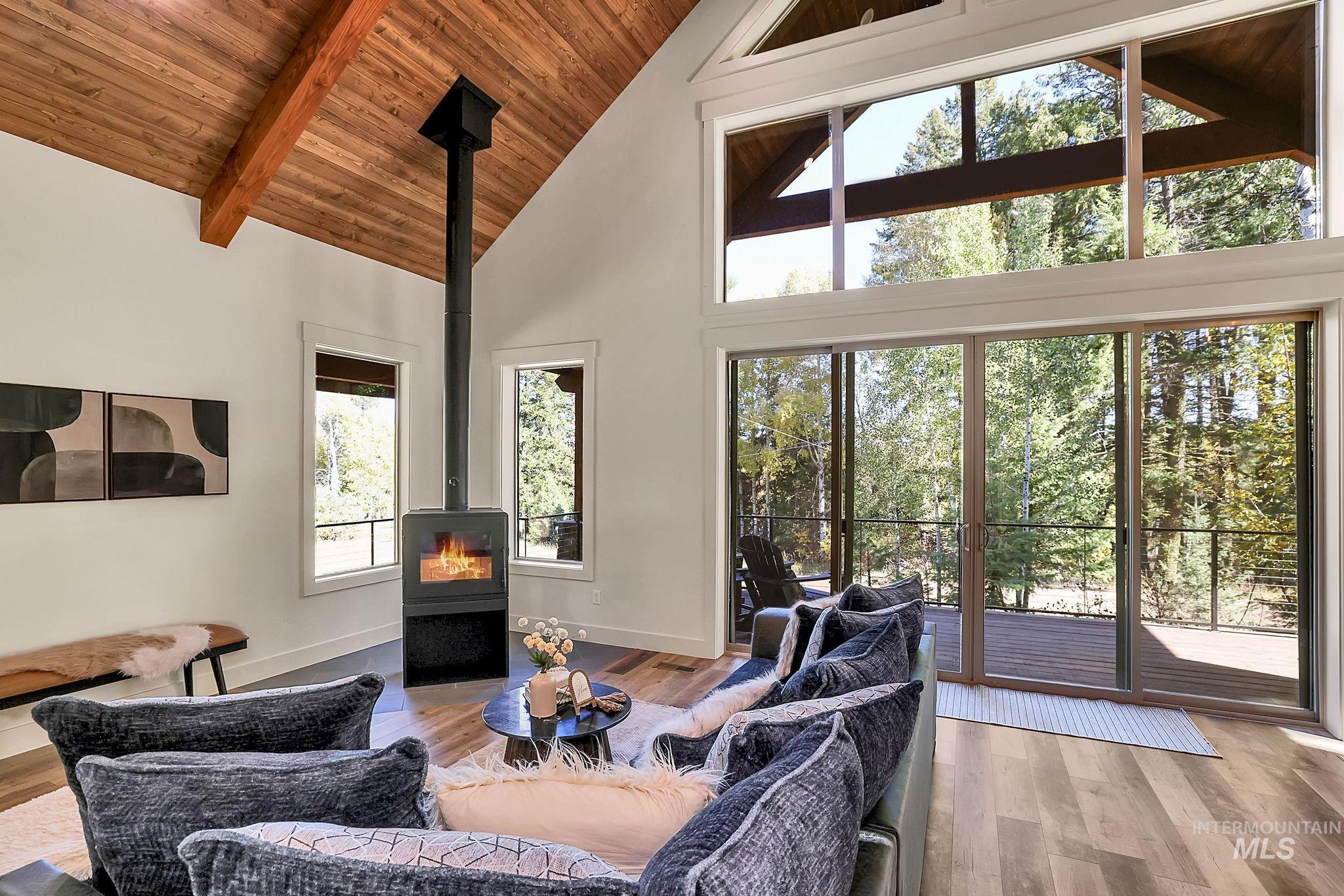 Living room with a wood stove, high vaulted ceiling, a wood ceiling with exposed beams, and wood finished floors