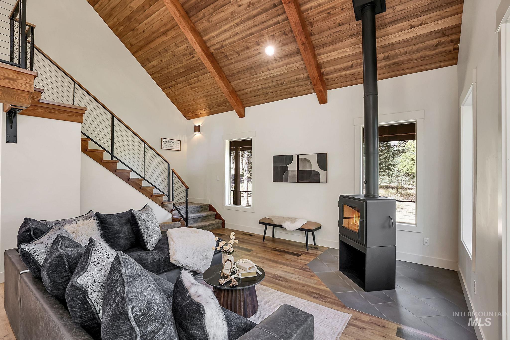 Living area featuring a wood stove, a wood ceiling with exposed beams, stairs, wood finished floors, and high vaulted ceiling