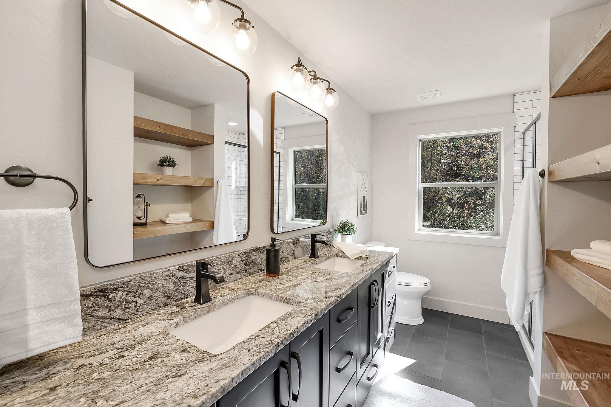Bathroom featuring double vanity, healthy amount of natural light, and dark tile patterned floors