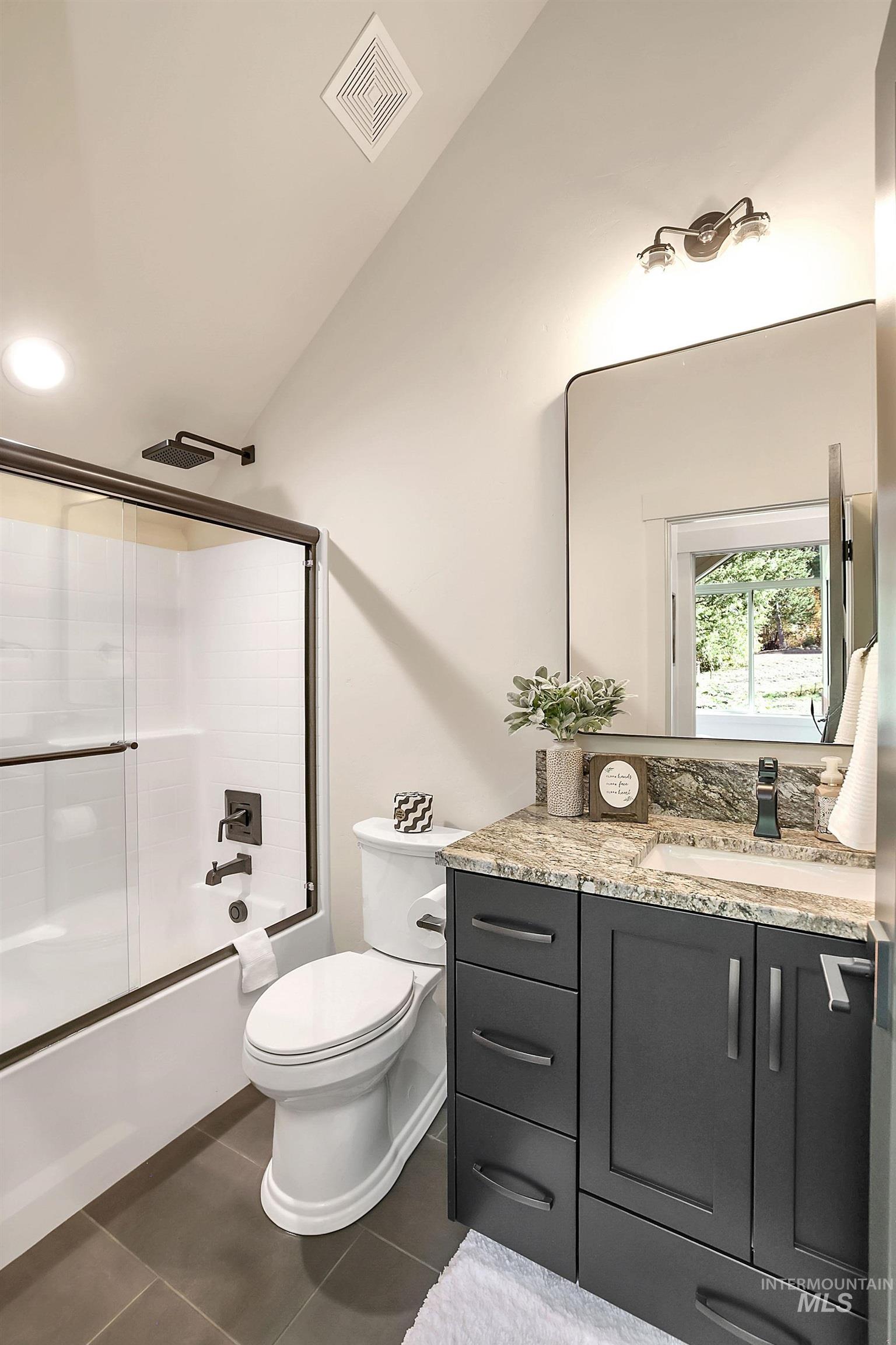 Bathroom with vanity, bath / shower combo with glass door, and dark tile patterned floors
