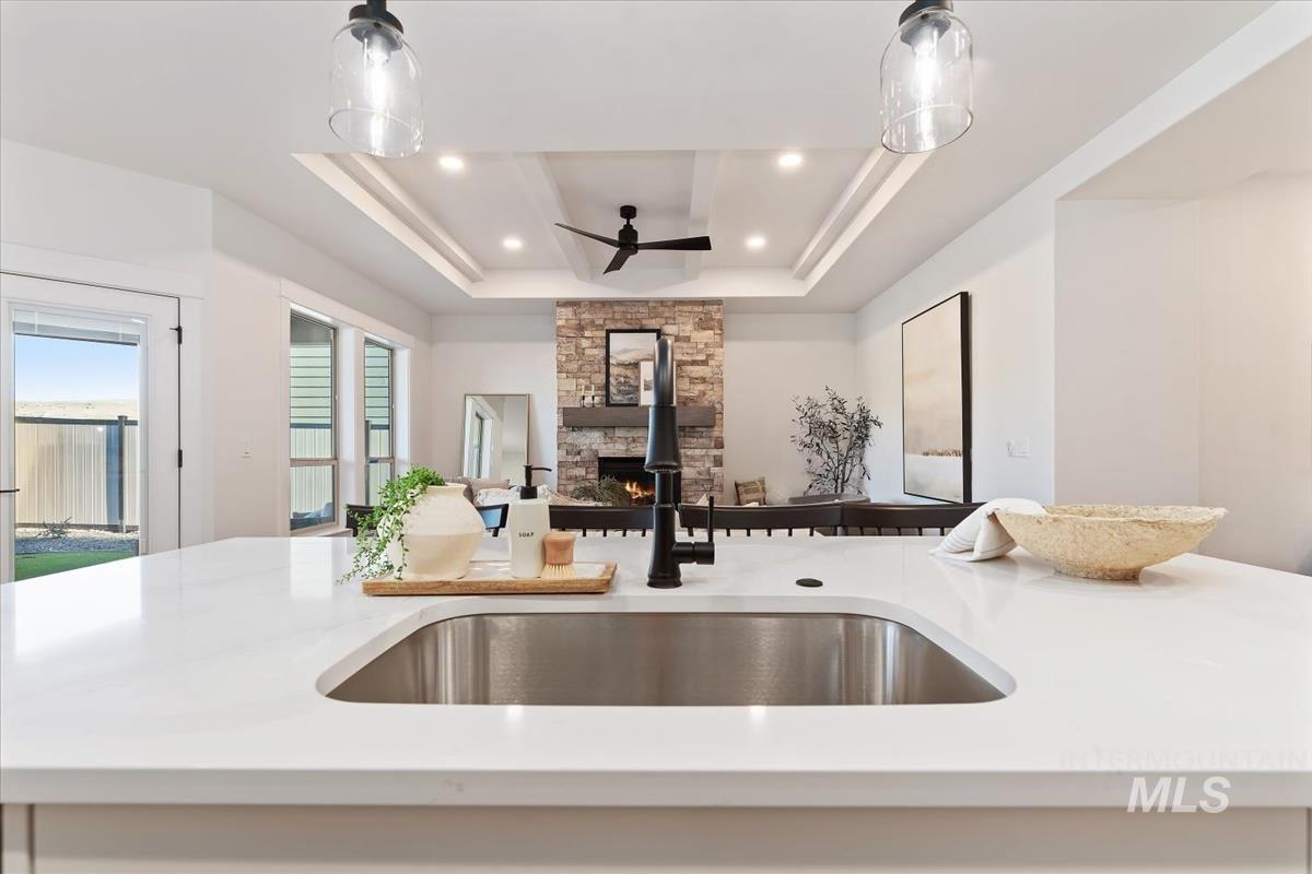 Kitchen featuring a raised ceiling, open floor plan, a ceiling fan, pendant lighting, and recessed lighting