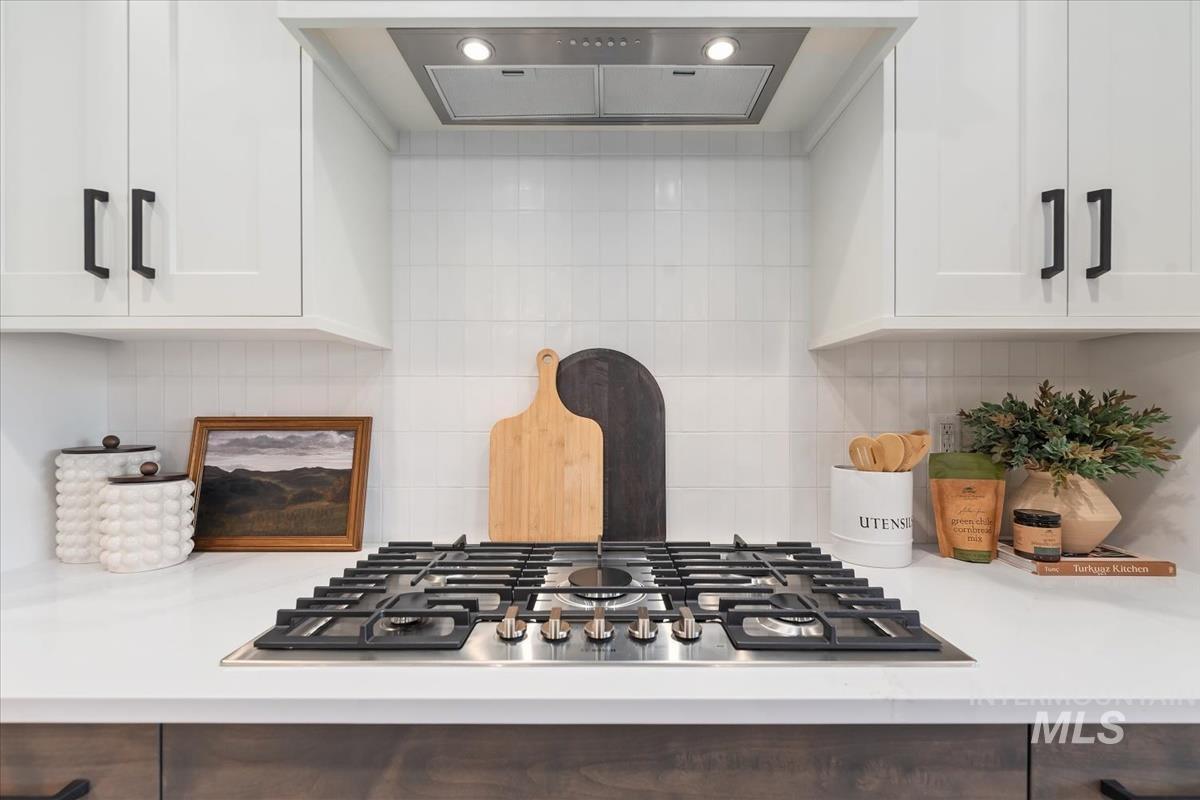Kitchen view of exhaust hood, light countertops, stainless steel gas stovetop, white cabinets, and tasteful backsplash