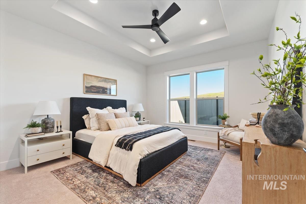 Bedroom with a raised ceiling, light colored carpet, recessed lighting, and a ceiling fan