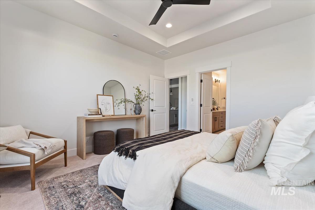 Carpeted bedroom with a ceiling fan, connected bathroom, and a tray ceiling