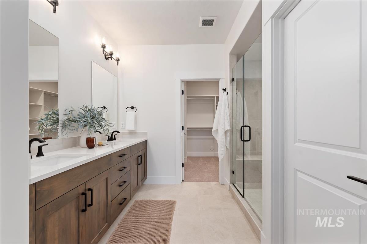 Full bath featuring double vanity, a walk in closet, a shower stall, and tile patterned floors