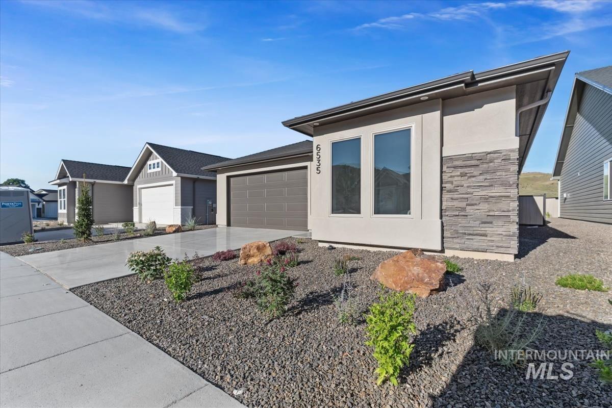 View of front of home featuring a garage, concrete driveway, stone siding, and stucco siding