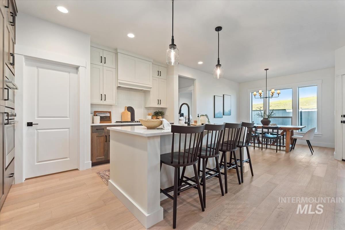Kitchen with a kitchen bar, light wood-style floors, a kitchen island with sink, backsplash, and recessed lighting