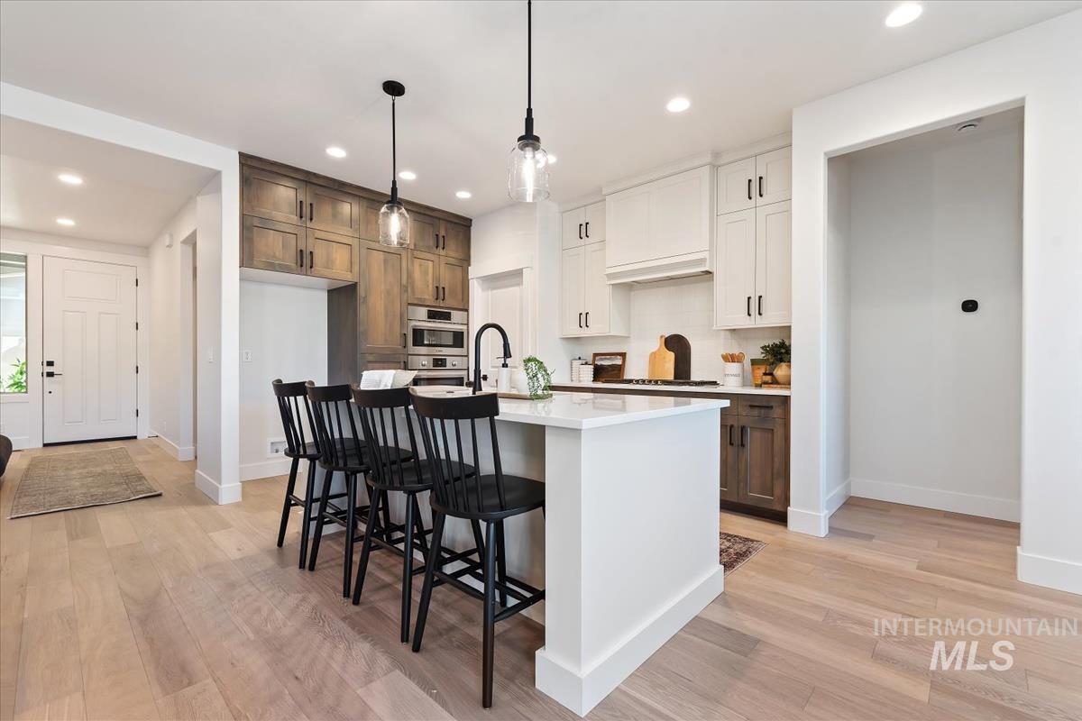 Kitchen featuring recessed lighting, light countertops, light wood-type flooring, a center island with sink, and a breakfast bar area