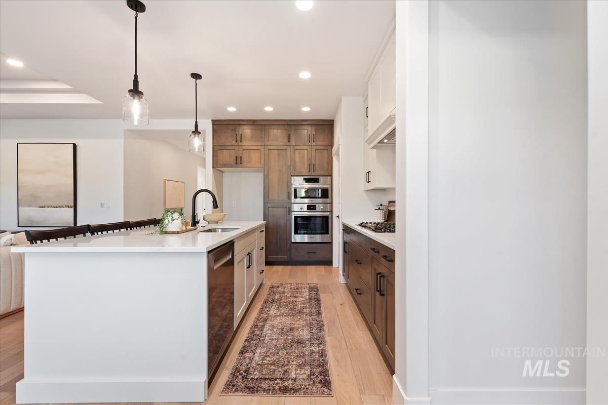 Kitchen featuring light wood finished floors, recessed lighting, light countertops, decorative light fixtures, and stainless steel appliances