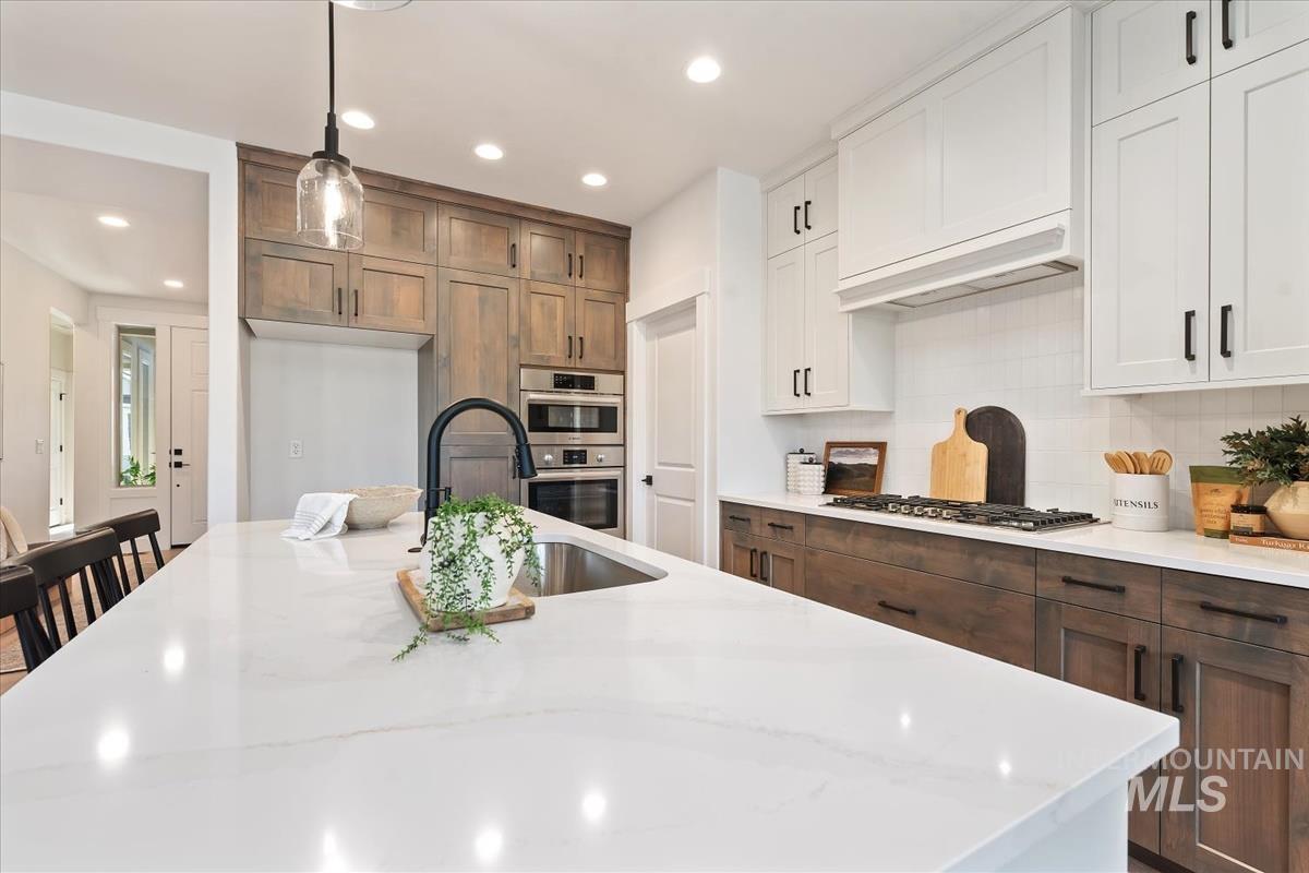 Kitchen with tasteful backsplash, pendant lighting, recessed lighting, white cabinets, and light stone counters
