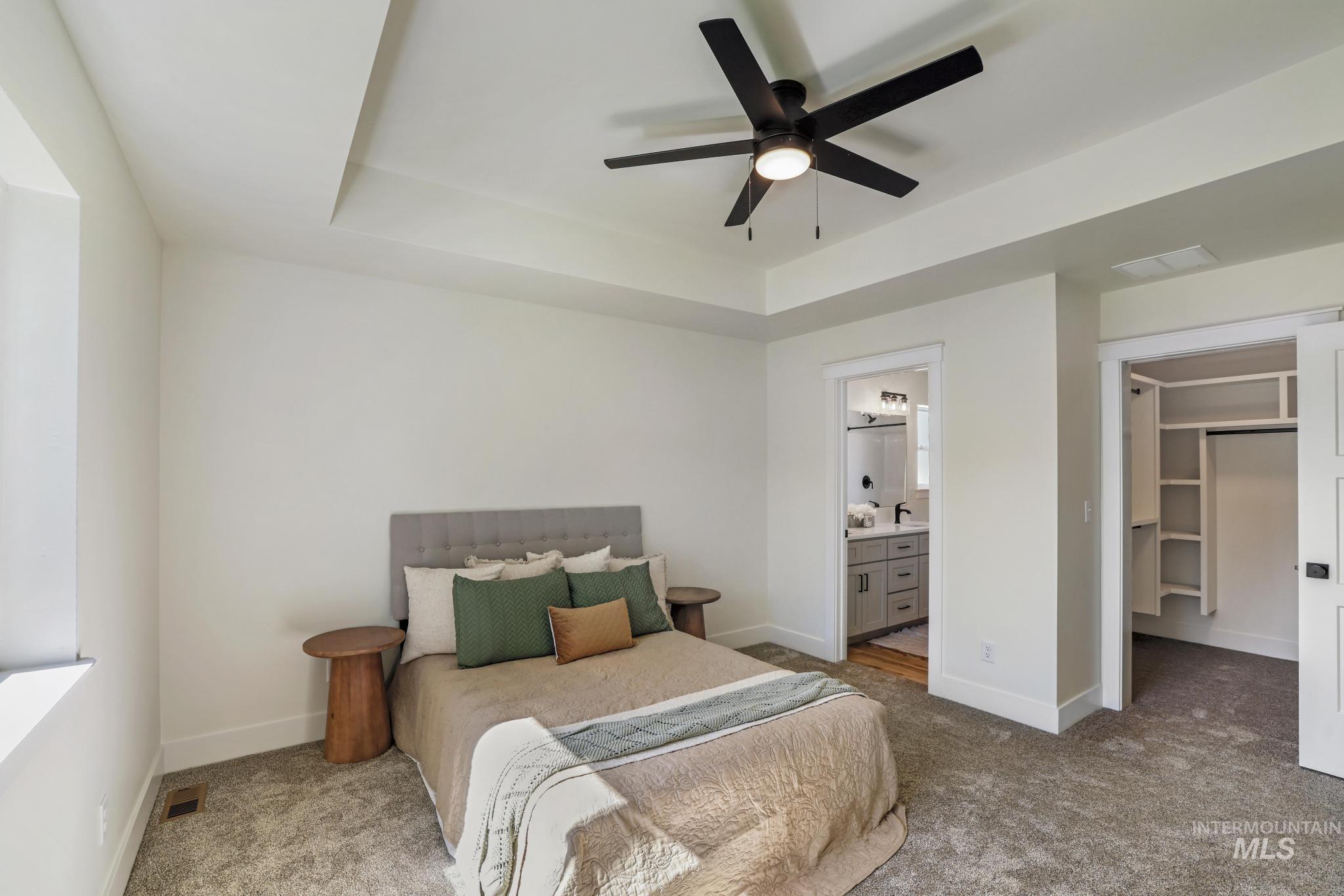 Carpeted bedroom featuring a tray ceiling, a spacious closet, a ceiling fan, and ensuite bath