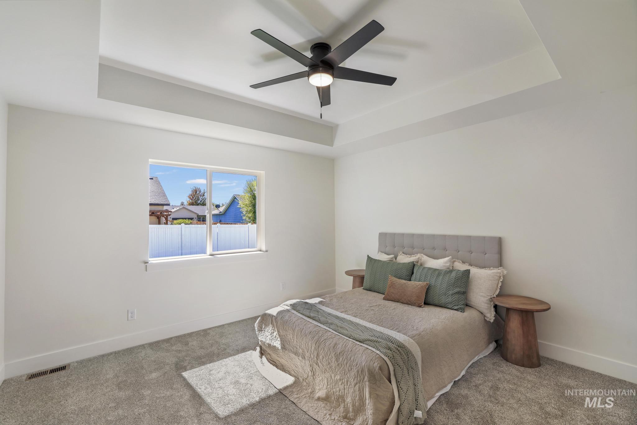 Bedroom featuring a raised ceiling, carpet floors, and a ceiling fan