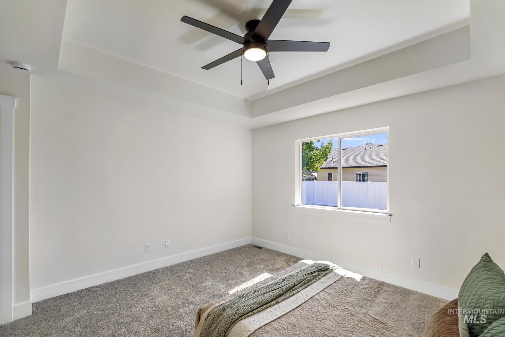 Unfurnished bedroom featuring a raised ceiling, carpet flooring, and ceiling fan