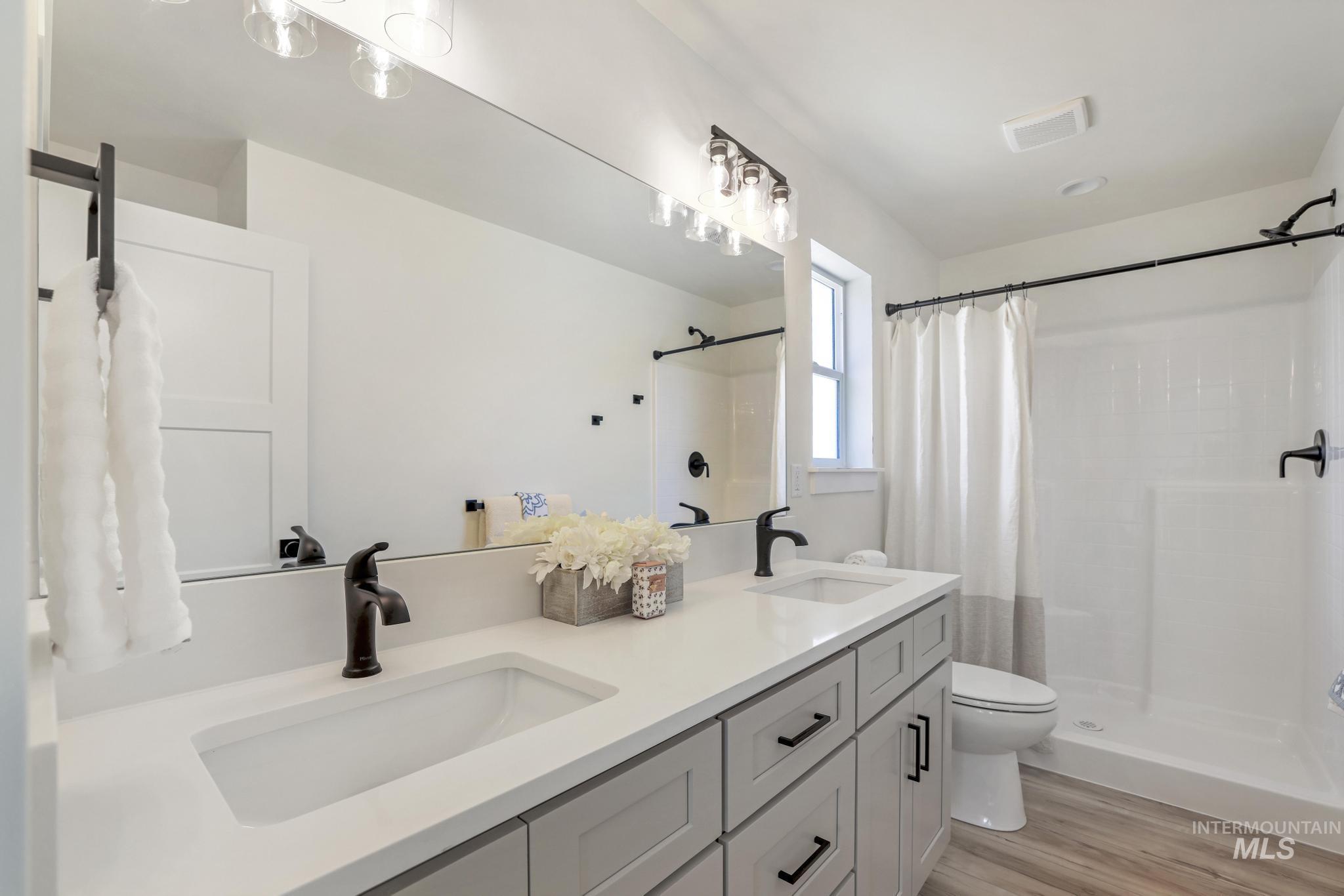 Bathroom featuring light wood finished floors, double vanity, and a shower stall