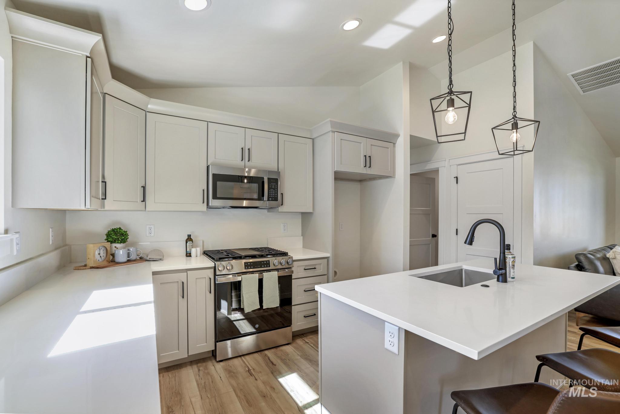 Kitchen featuring lofted ceiling, stainless steel appliances, a center island with sink, a kitchen bar, and decorative light fixtures