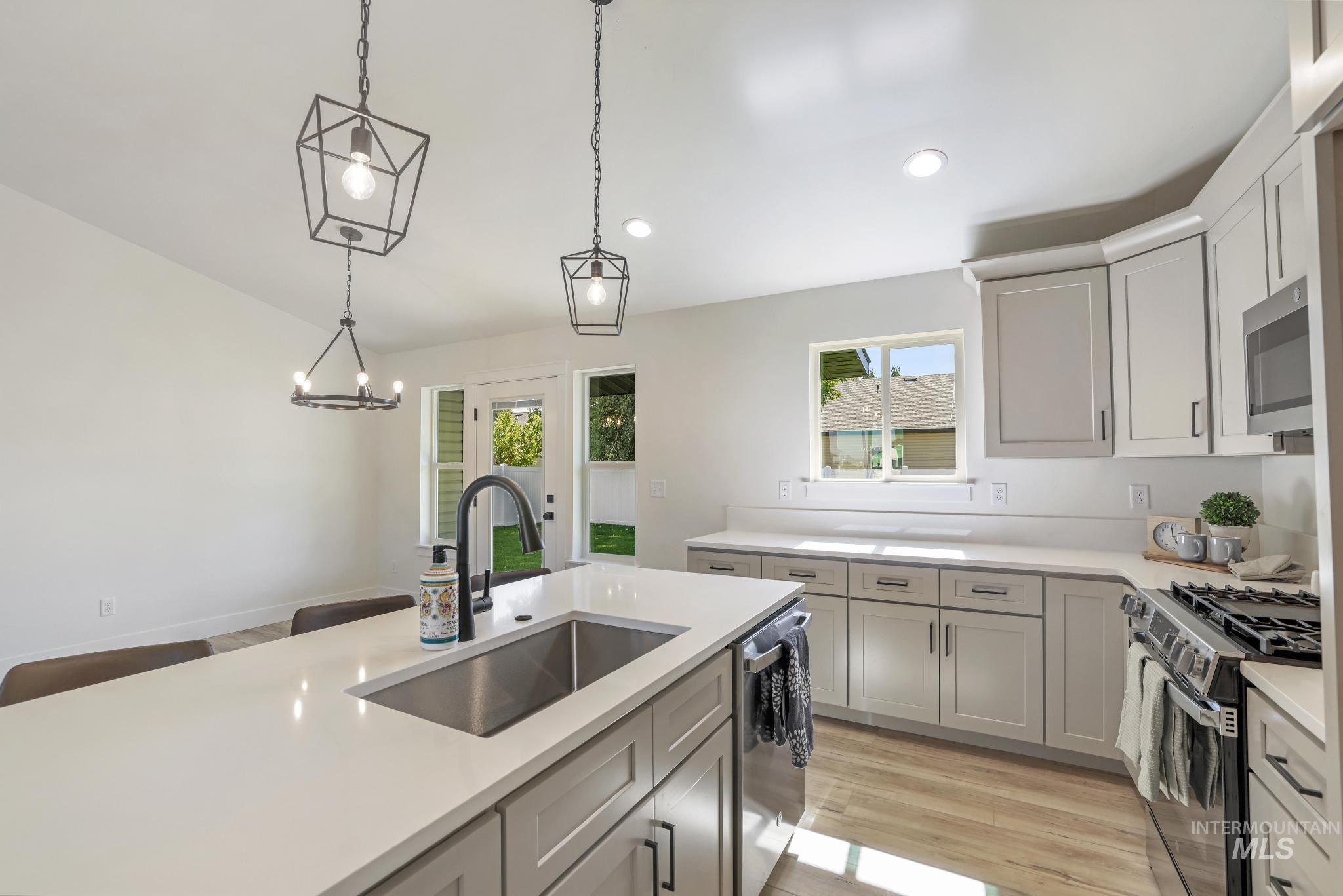 Kitchen featuring light wood-style flooring, appliances with stainless steel finishes, decorative light fixtures, gray cabinetry, and recessed lighting