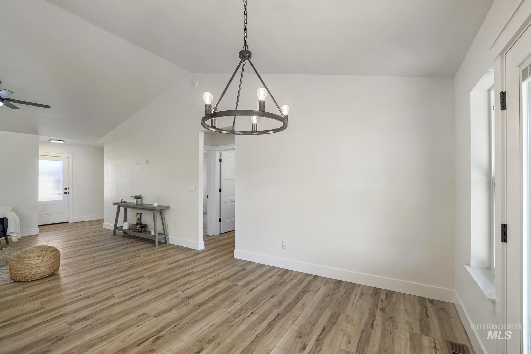 Unfurnished dining area with light wood-style flooring, lofted ceiling, a chandelier, and a ceiling fan