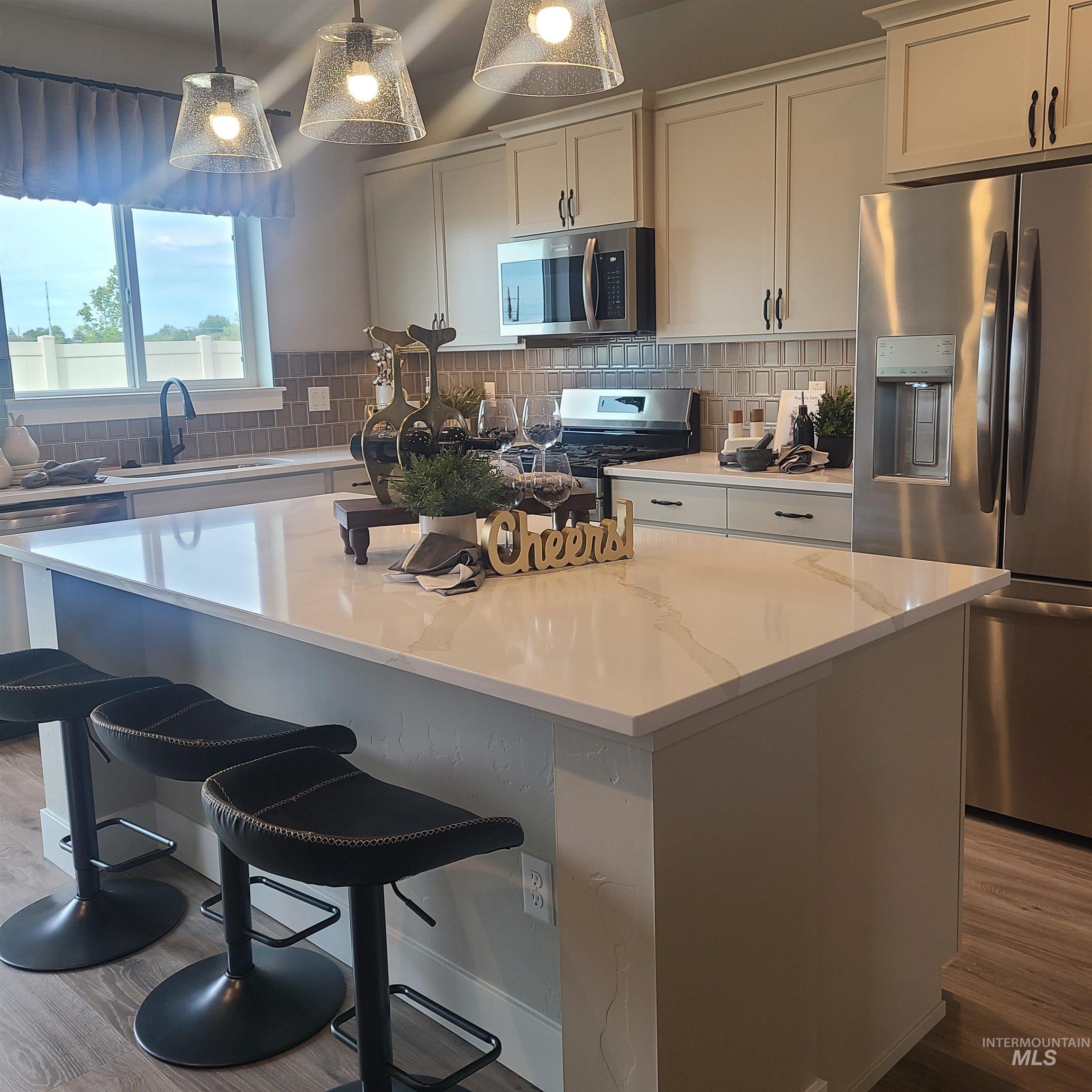 Kitchen featuring appliances with stainless steel finishes, backsplash, light wood-type flooring, and hanging light fixtures