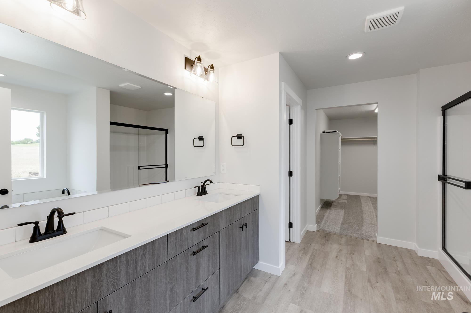 Bathroom featuring a walk in closet, double vanity, a stall shower, wood finished floors, and recessed lighting