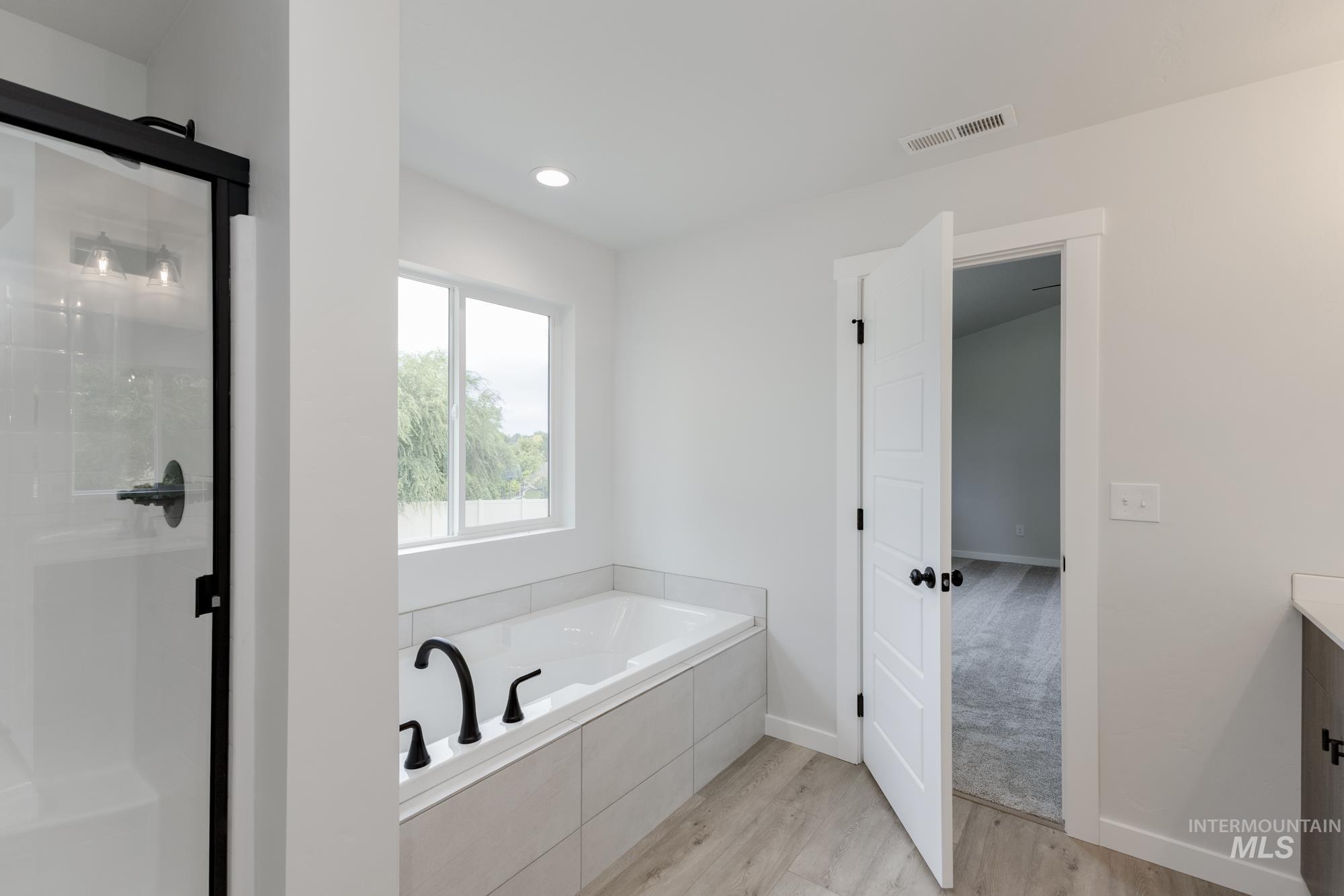 Bathroom with wood finished floors, a shower stall, a garden tub, vanity, and recessed lighting