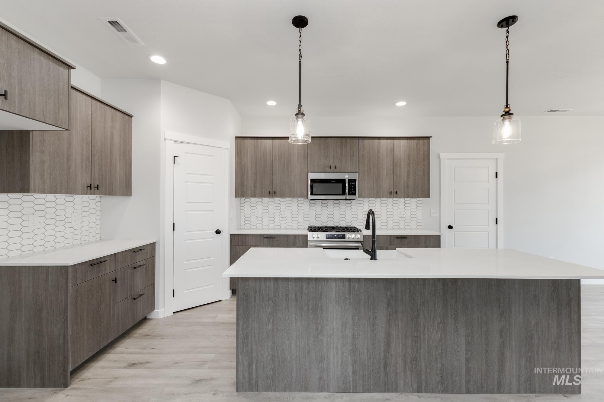 Kitchen featuring stainless steel appliances, modern cabinets, backsplash, light wood finished floors, and light countertops