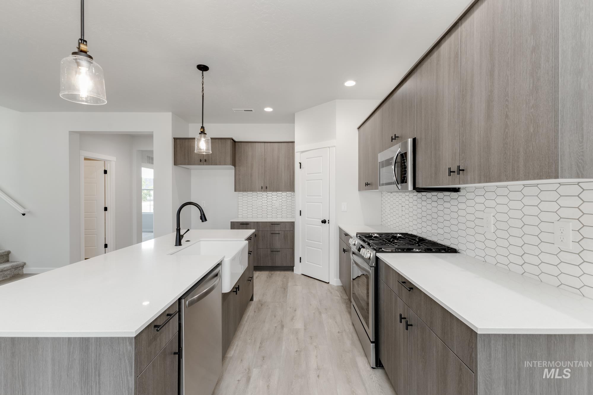 Kitchen with stainless steel appliances, modern cabinets, light wood-style flooring, tasteful backsplash, and light countertops