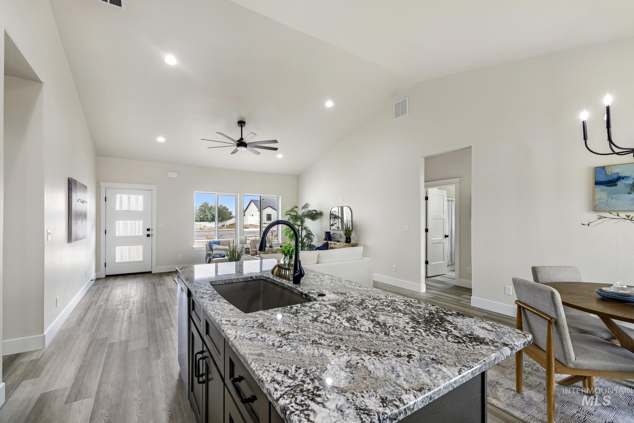 Kitchen featuring light stone counters, light wood-type flooring, recessed lighting, an island with sink, and dark cabinets