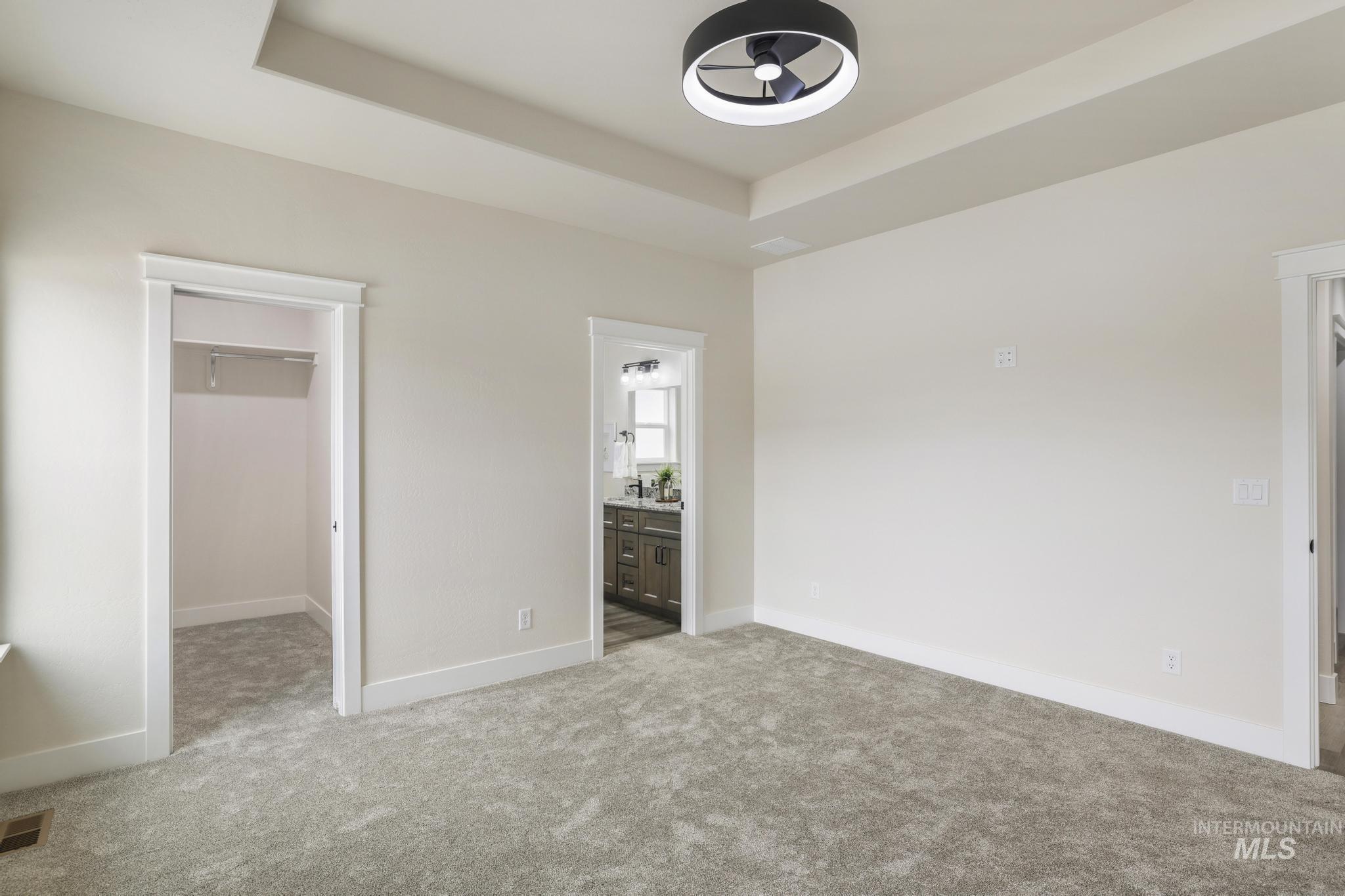 Unfurnished bedroom featuring a raised ceiling, a spacious closet, light carpet, and connected bathroom