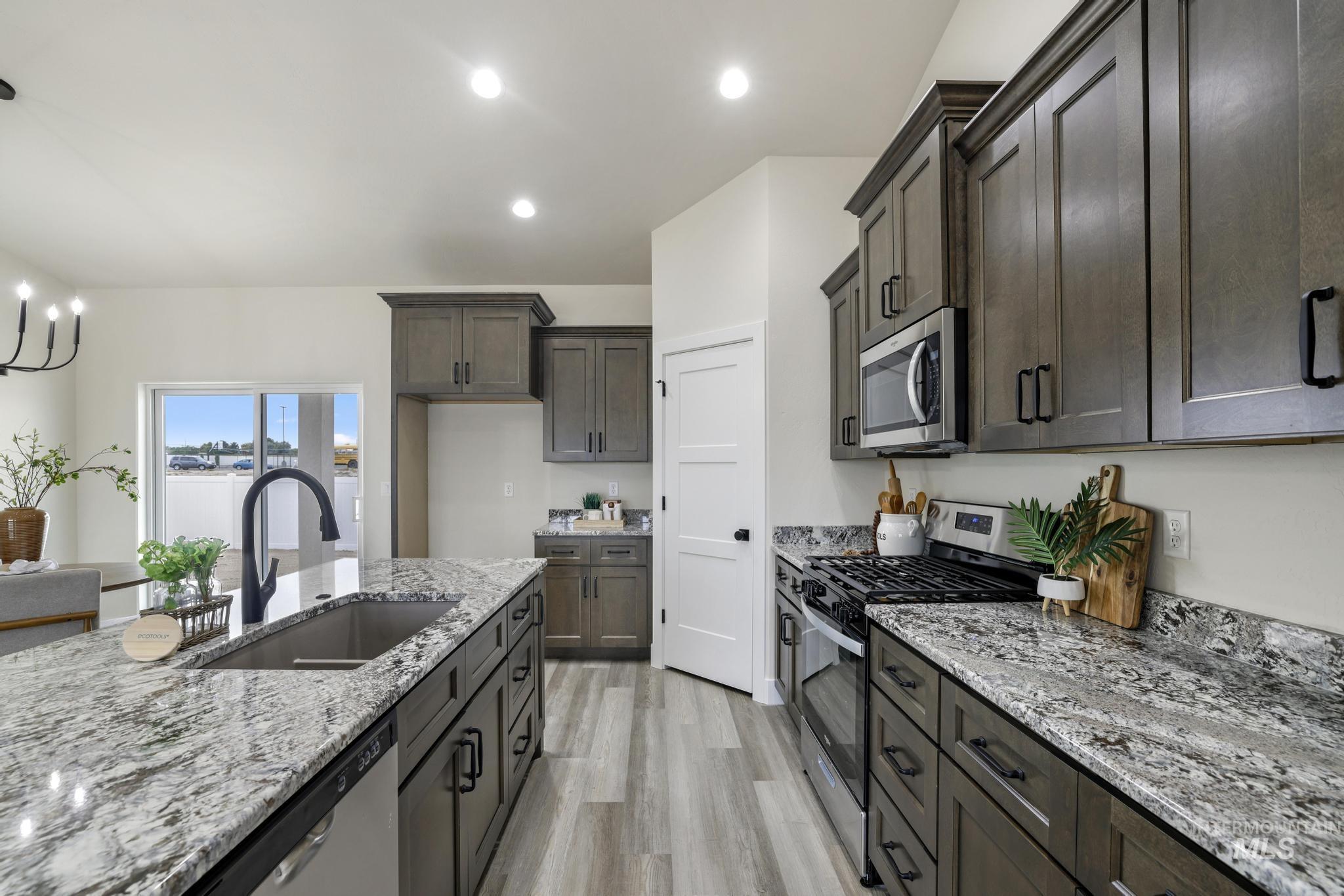 Kitchen with appliances with stainless steel finishes, light wood finished floors, light stone countertops, recessed lighting, and pendant lighting