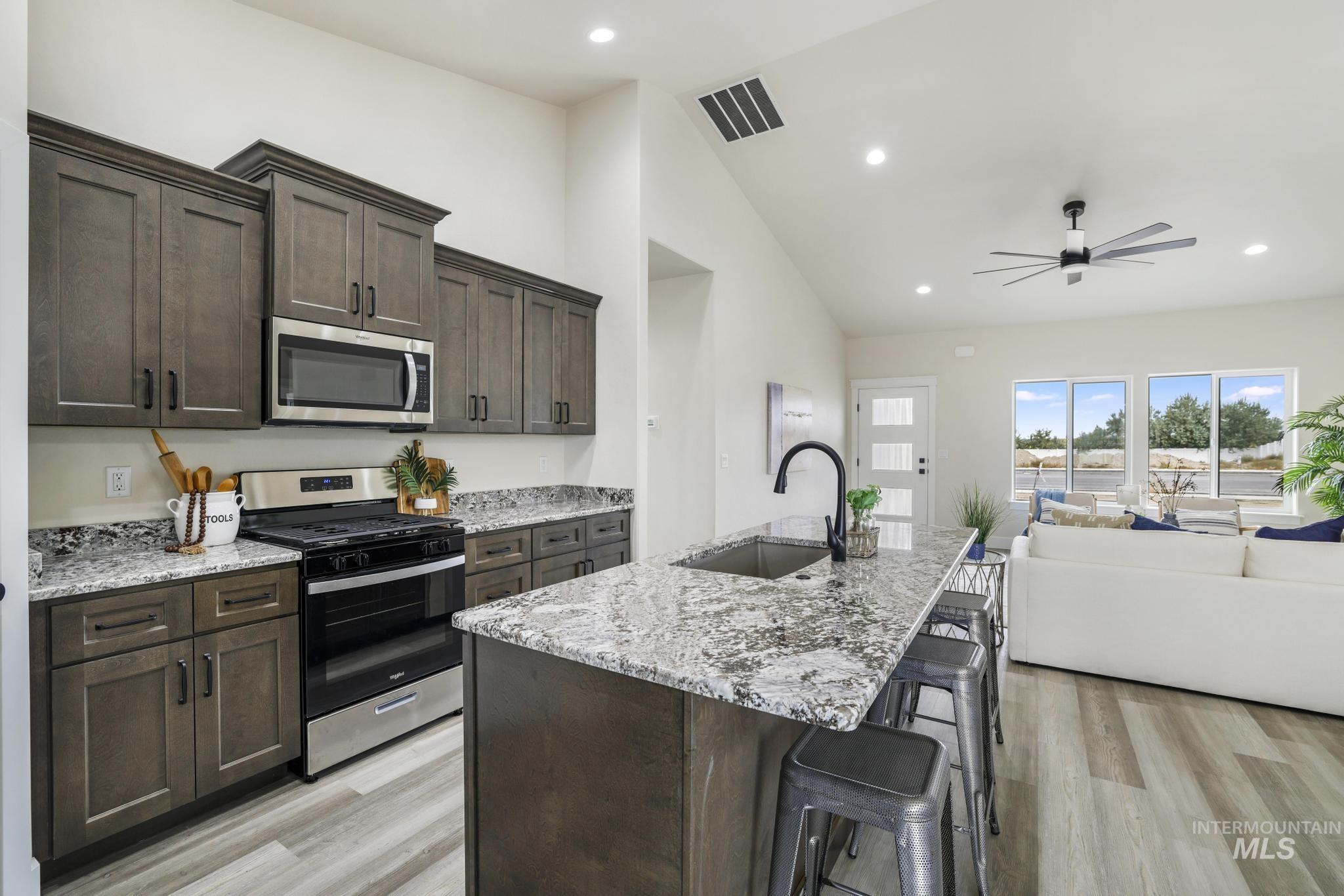Kitchen featuring dark brown cabinets, stainless steel appliances, light stone countertops, recessed lighting, and high vaulted ceiling