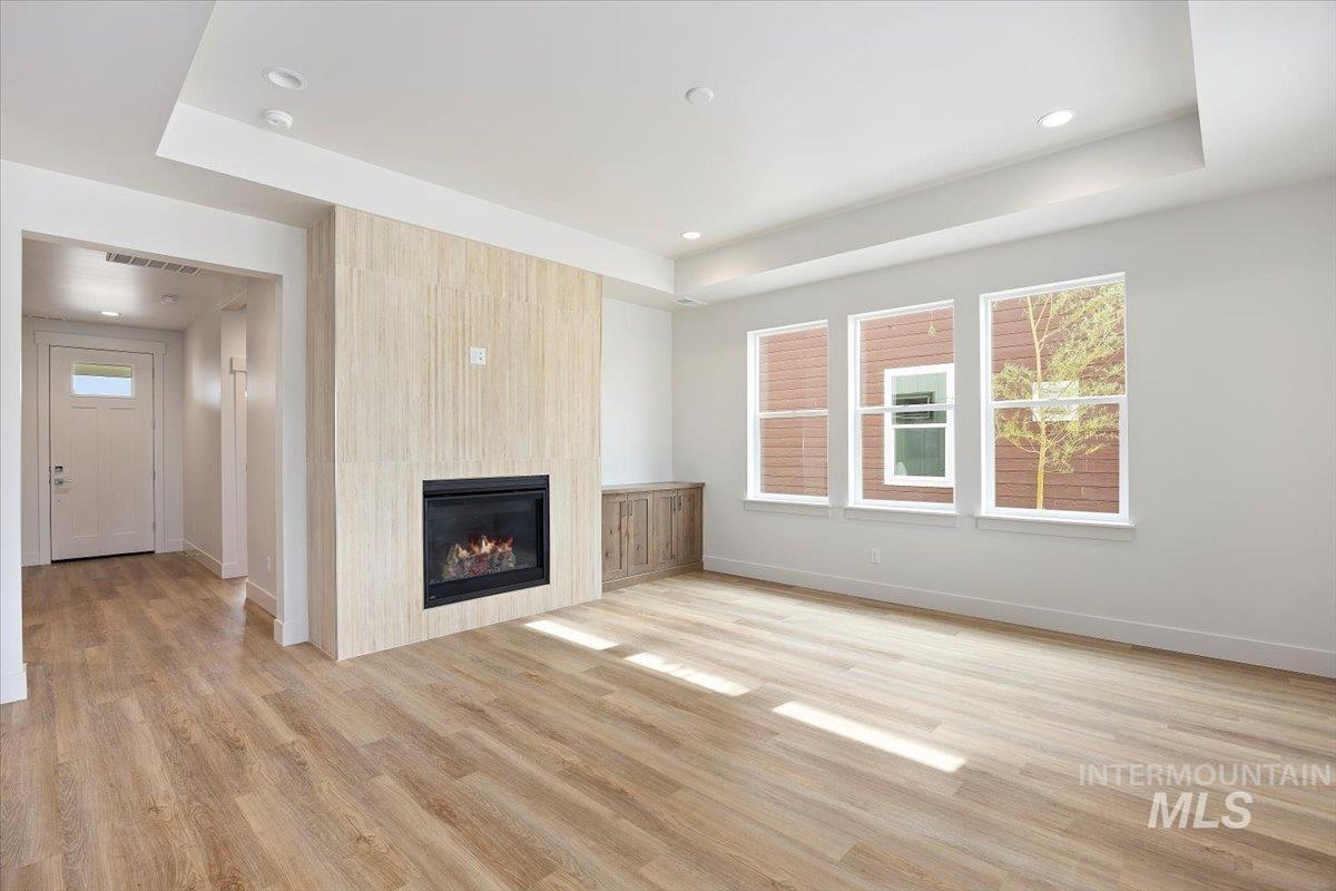 Unfurnished living room featuring light wood finished floors, a large fireplace, a tray ceiling, and recessed lighting