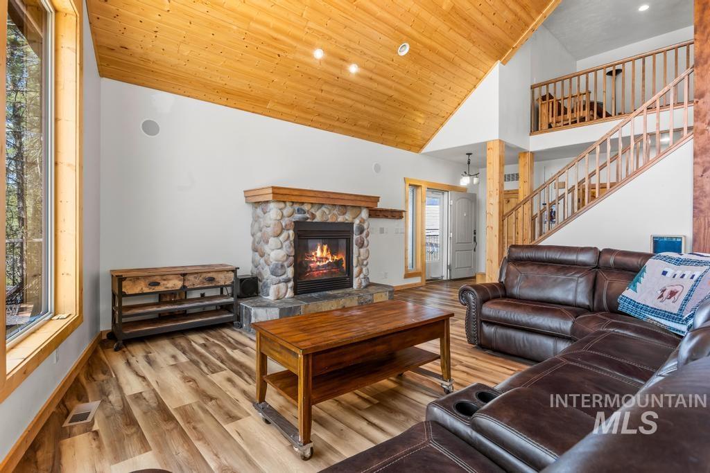 Living area with a fireplace, light wood-style flooring, wood ceiling, high vaulted ceiling, and stairway