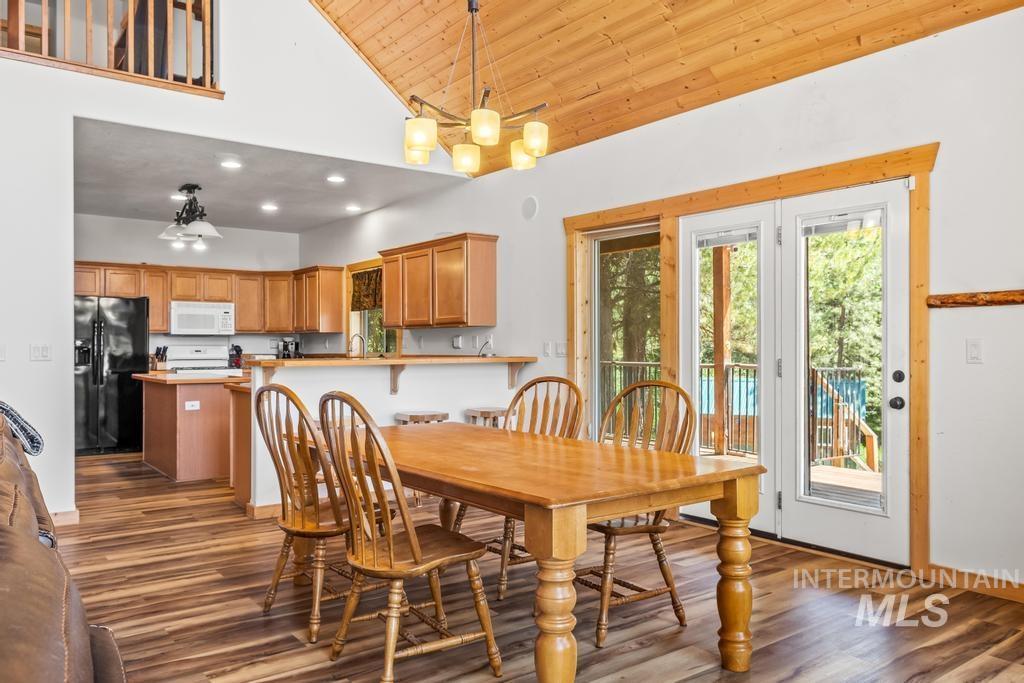 Dining area featuring high vaulted ceiling, dark wood-style flooring, a chandelier, wooden ceiling, and recessed lighting