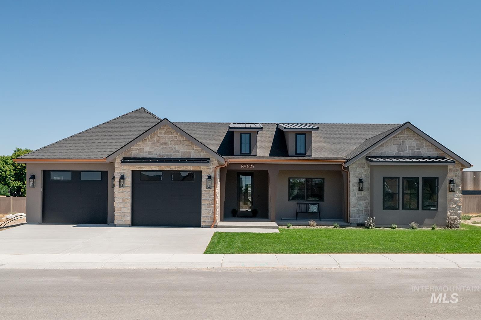 View of front facade featuring stone siding, a garage, concrete driveway, a standing seam roof, and a front yard