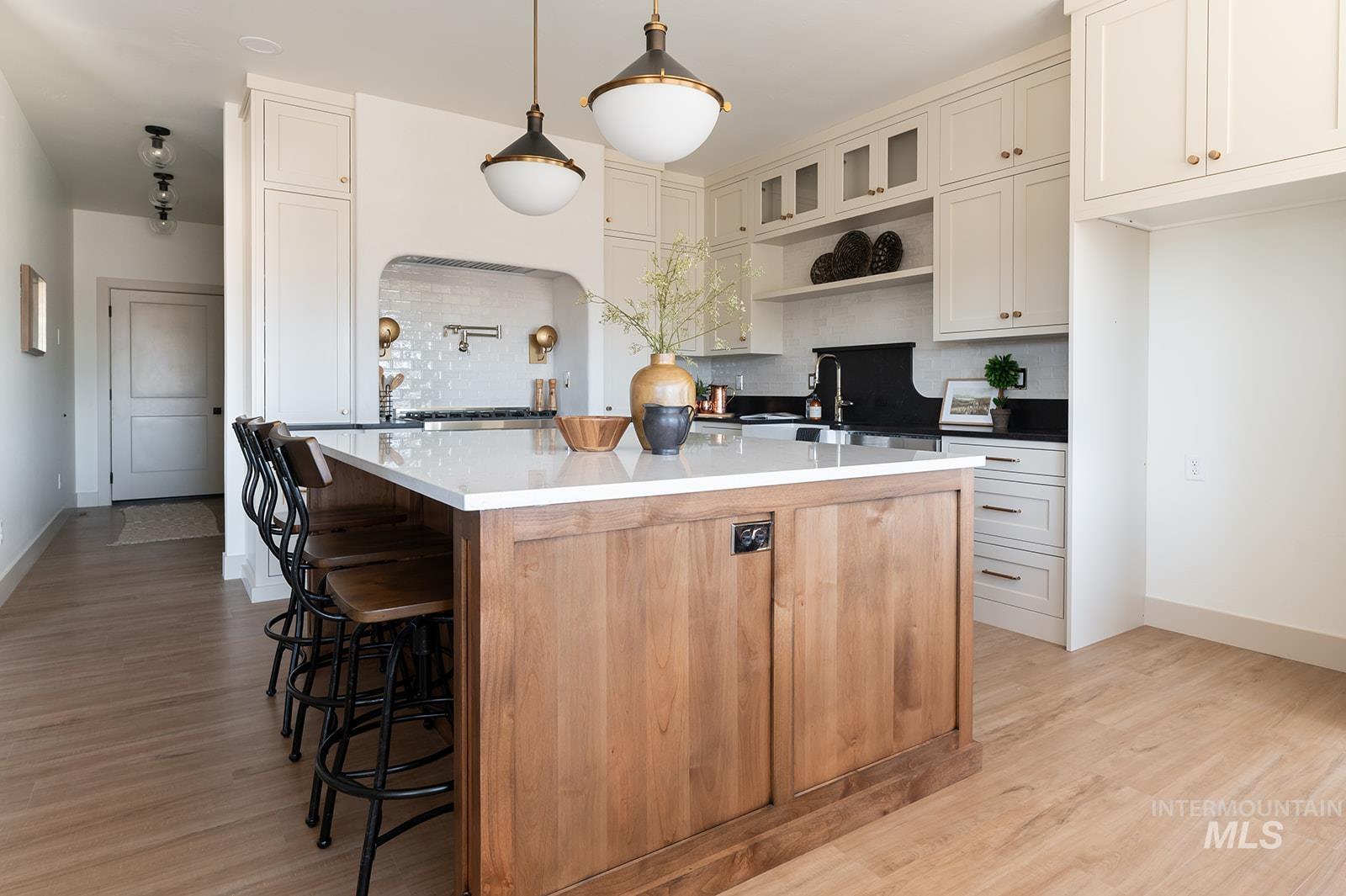 Kitchen featuring decorative backsplash, open shelves, a center island, light wood finished floors, and a kitchen breakfast bar