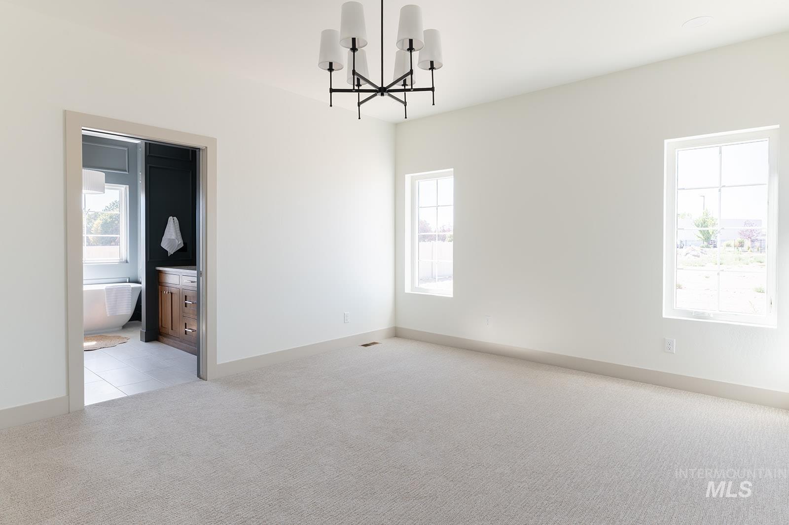 Spare room featuring light carpet, plenty of natural light, and a chandelier