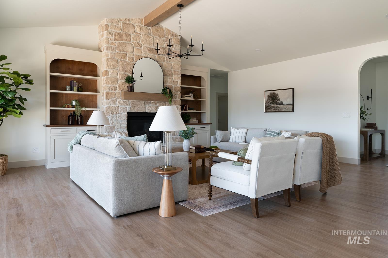 Living area with arched walkways, light wood-style floors, a stone fireplace, and built in features
