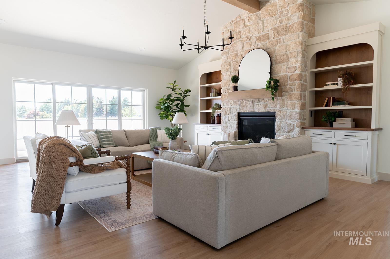 Living room with a fireplace, light wood-style flooring, a chandelier, beam ceiling, and high vaulted ceiling