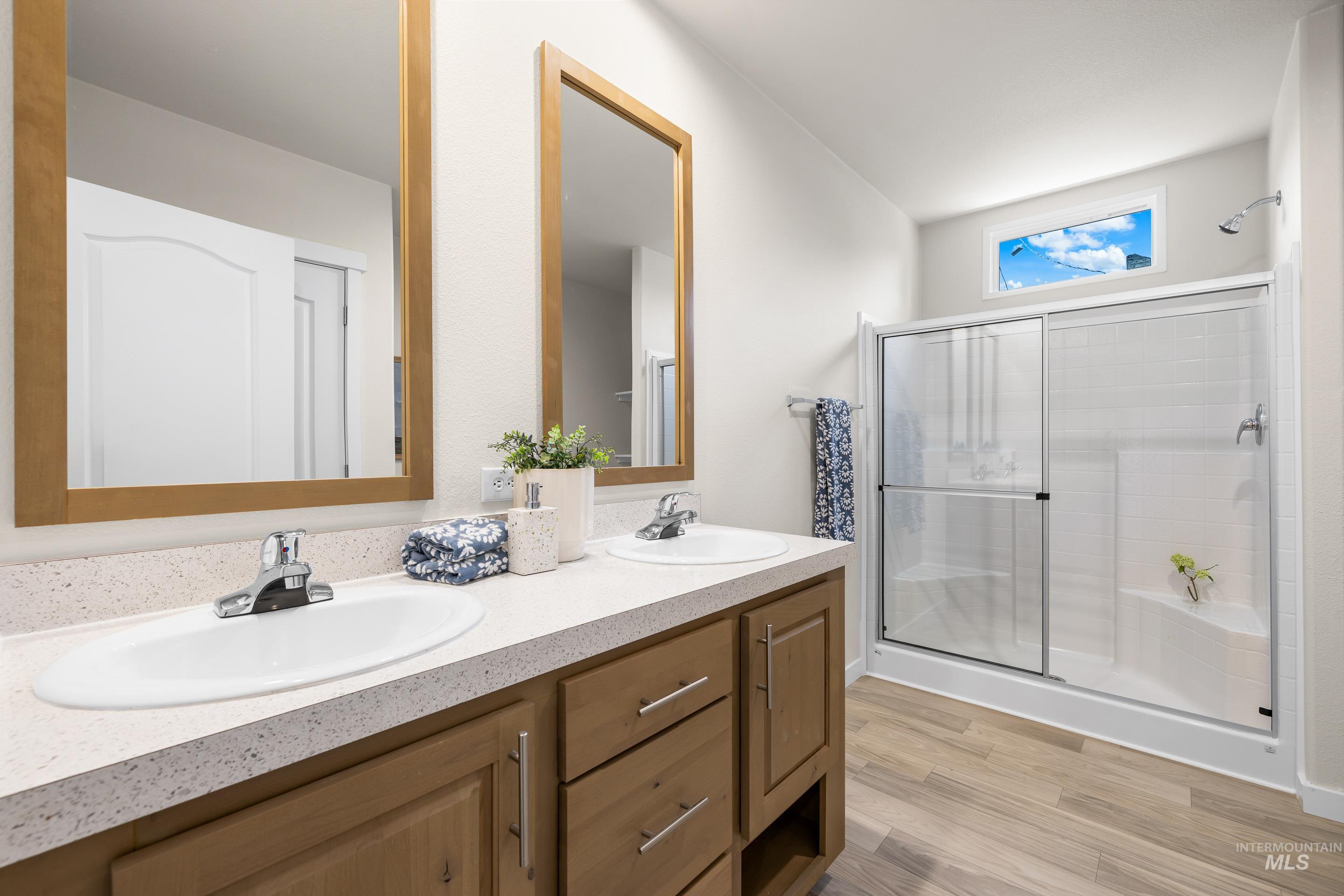 Full bath featuring a stall shower, double vanity, and wood finished floors