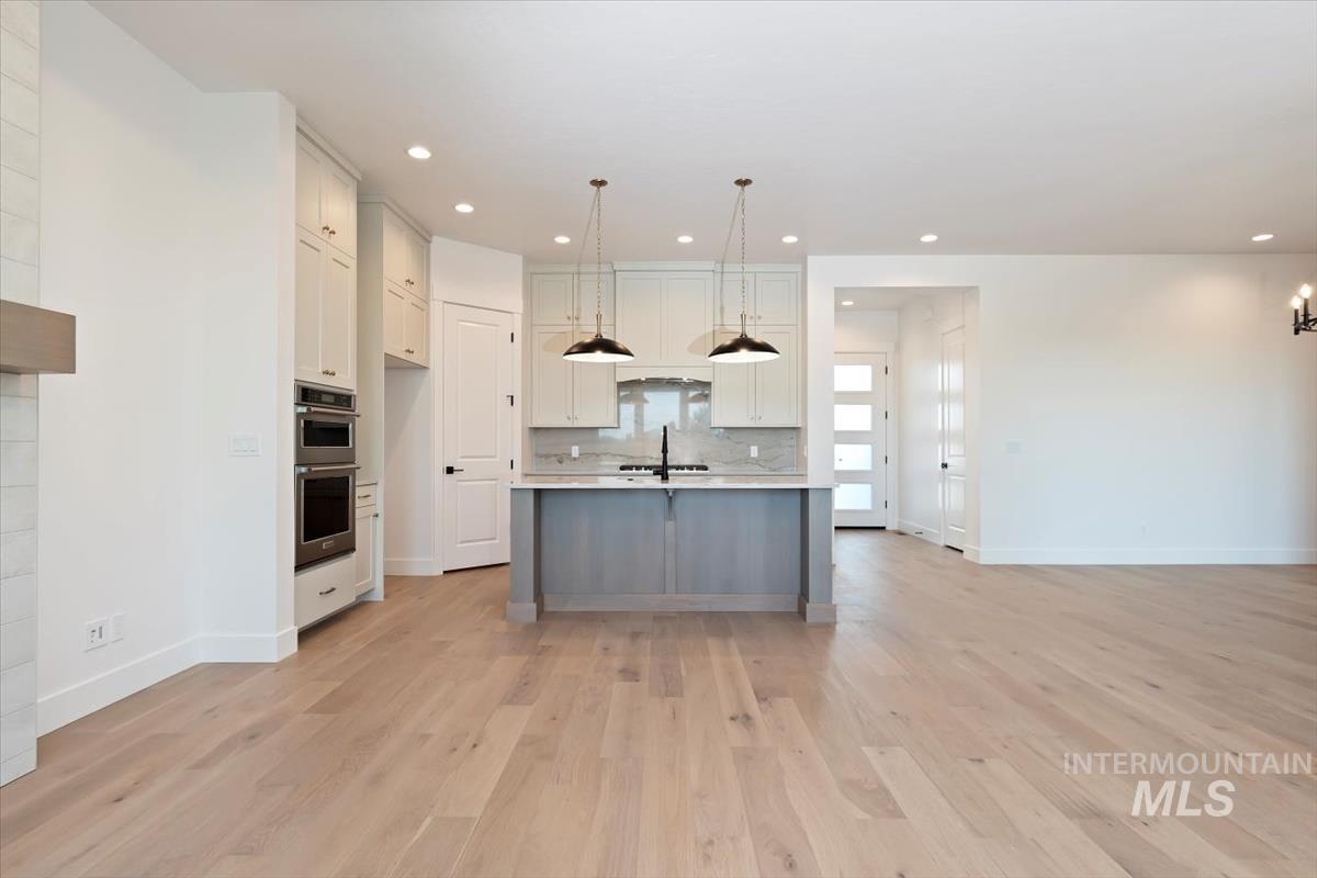 Kitchen featuring light countertops, decorative light fixtures, open floor plan, white cabinets, and light wood-style flooring