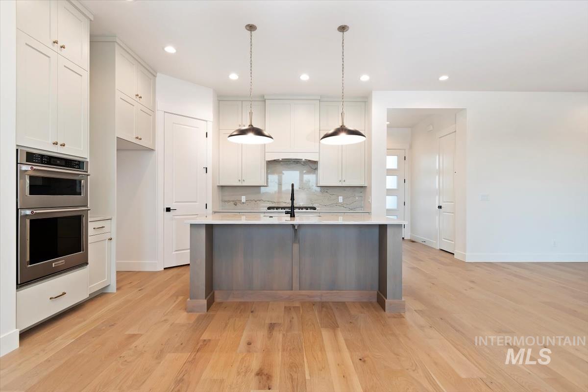Kitchen with tasteful backsplash, decorative light fixtures, double oven, recessed lighting, and white cabinetry