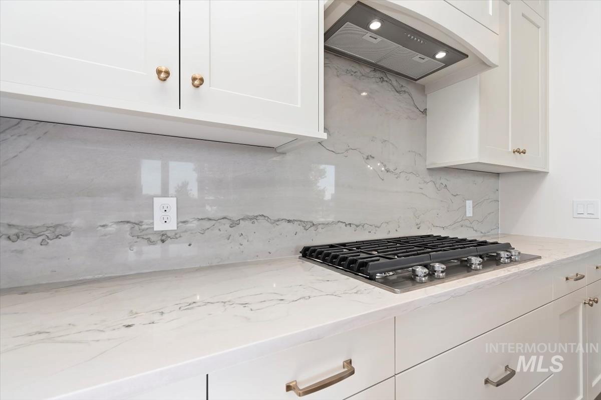 Kitchen with white cabinetry, light stone counters, custom exhaust hood, and decorative backsplash