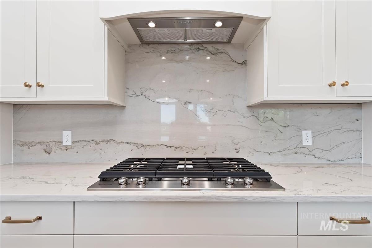 Kitchen featuring extractor fan, decorative backsplash, stainless steel gas cooktop, and white cabinetry