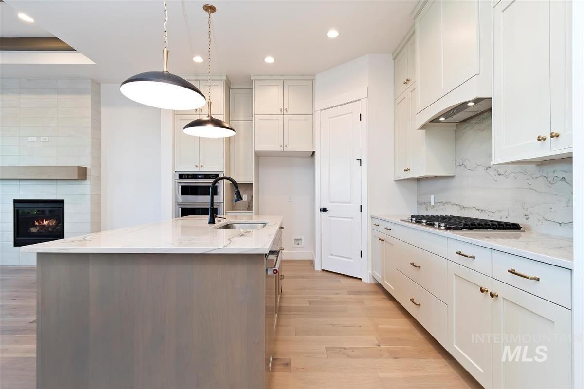 Kitchen featuring a kitchen island with sink, light stone counters, light wood-type flooring, decorative light fixtures, and recessed lighting