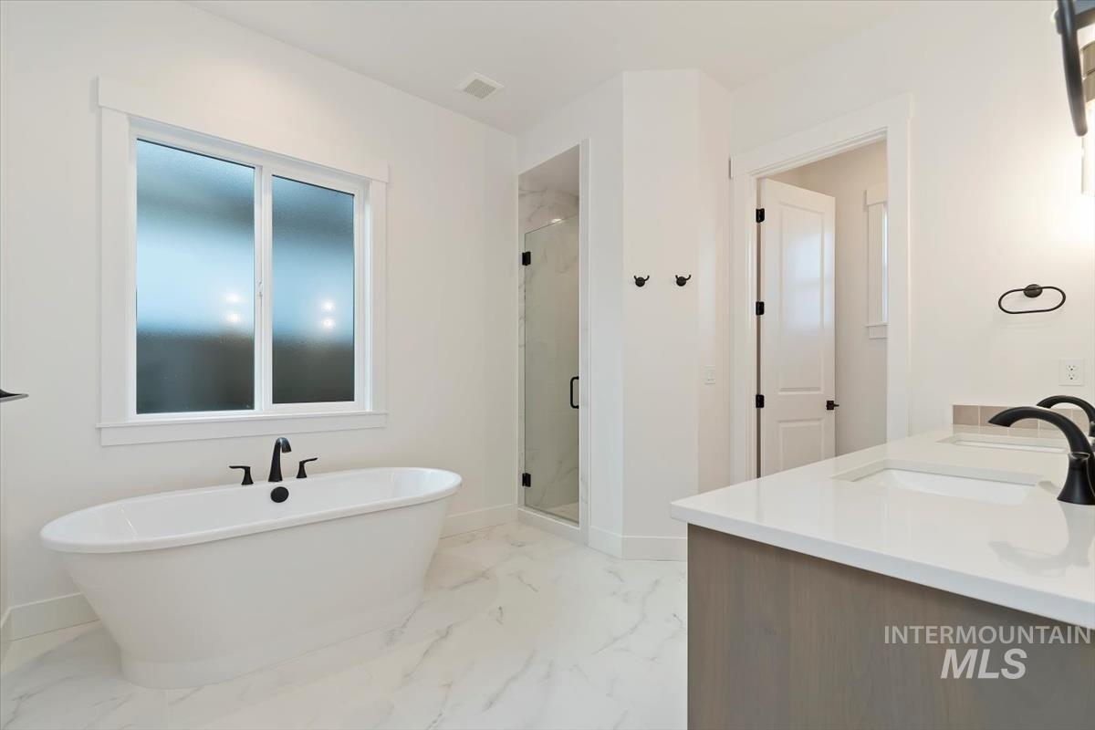 Full bath featuring a marble finish shower, double vanity, a soaking tub, and light marble finish floors